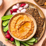 Roasted red pepper and feta dip in a serving bowl alongside vegetable sticks and crackers.