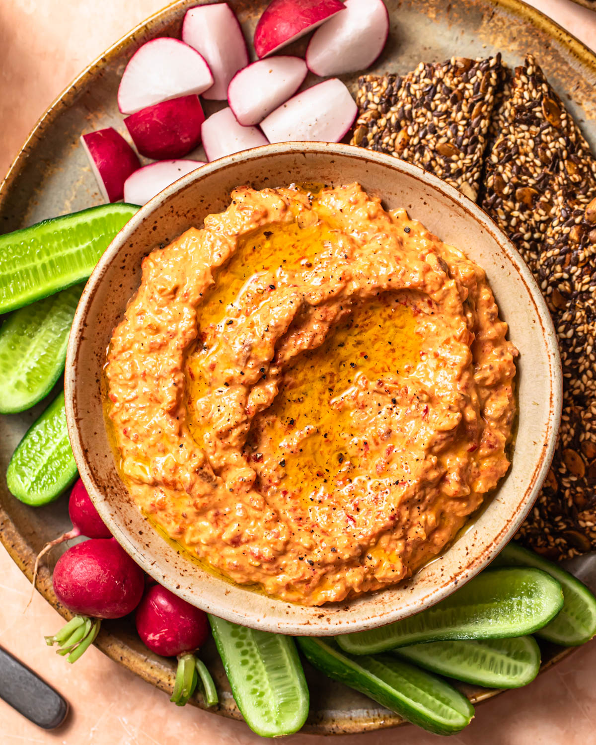 Close up photo of roasted red pepper and feta dip in a serving bowl alongside vegetable sticks and crackers.