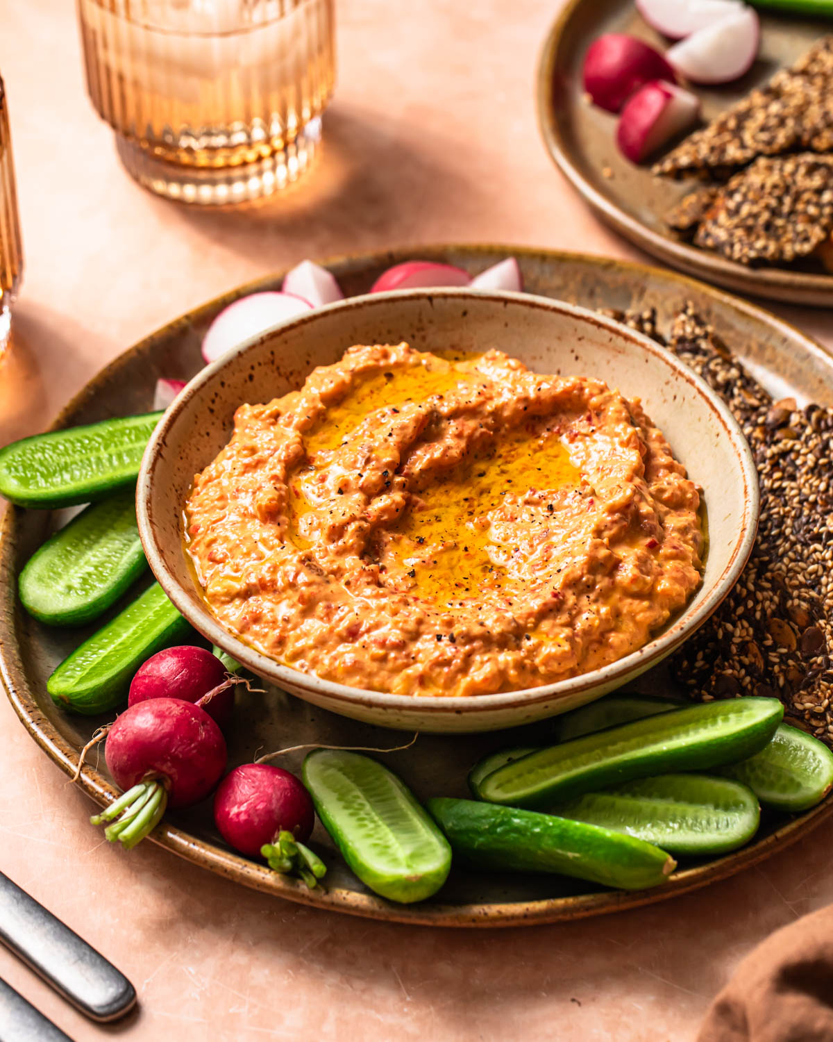 Front on photo of Roasted red pepper and feta dip in a serving bowl alongside vegetable sticks and crackers.