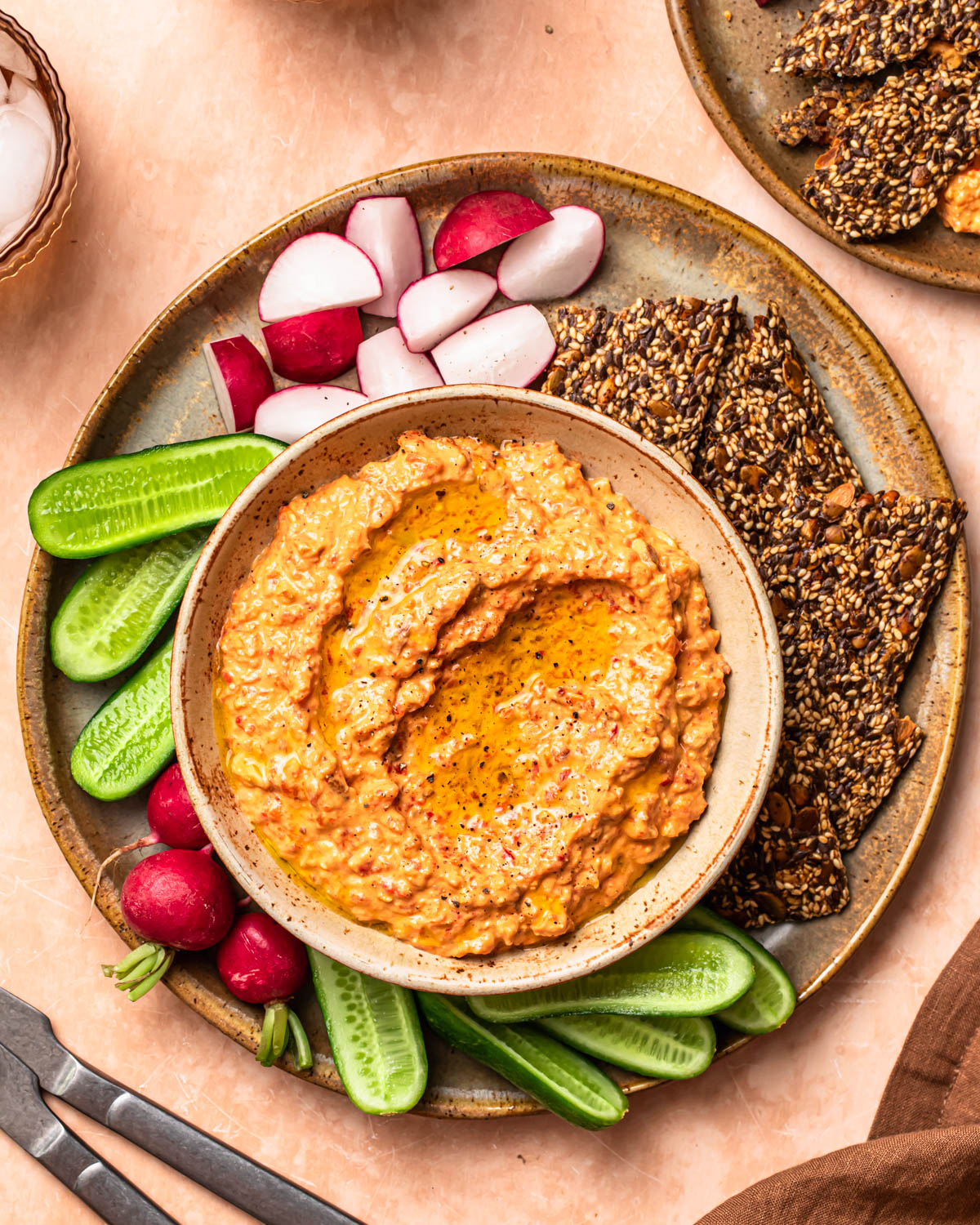 Roasted red pepper and feta dip in a serving bowl alongside vegetable sticks and crackers.
