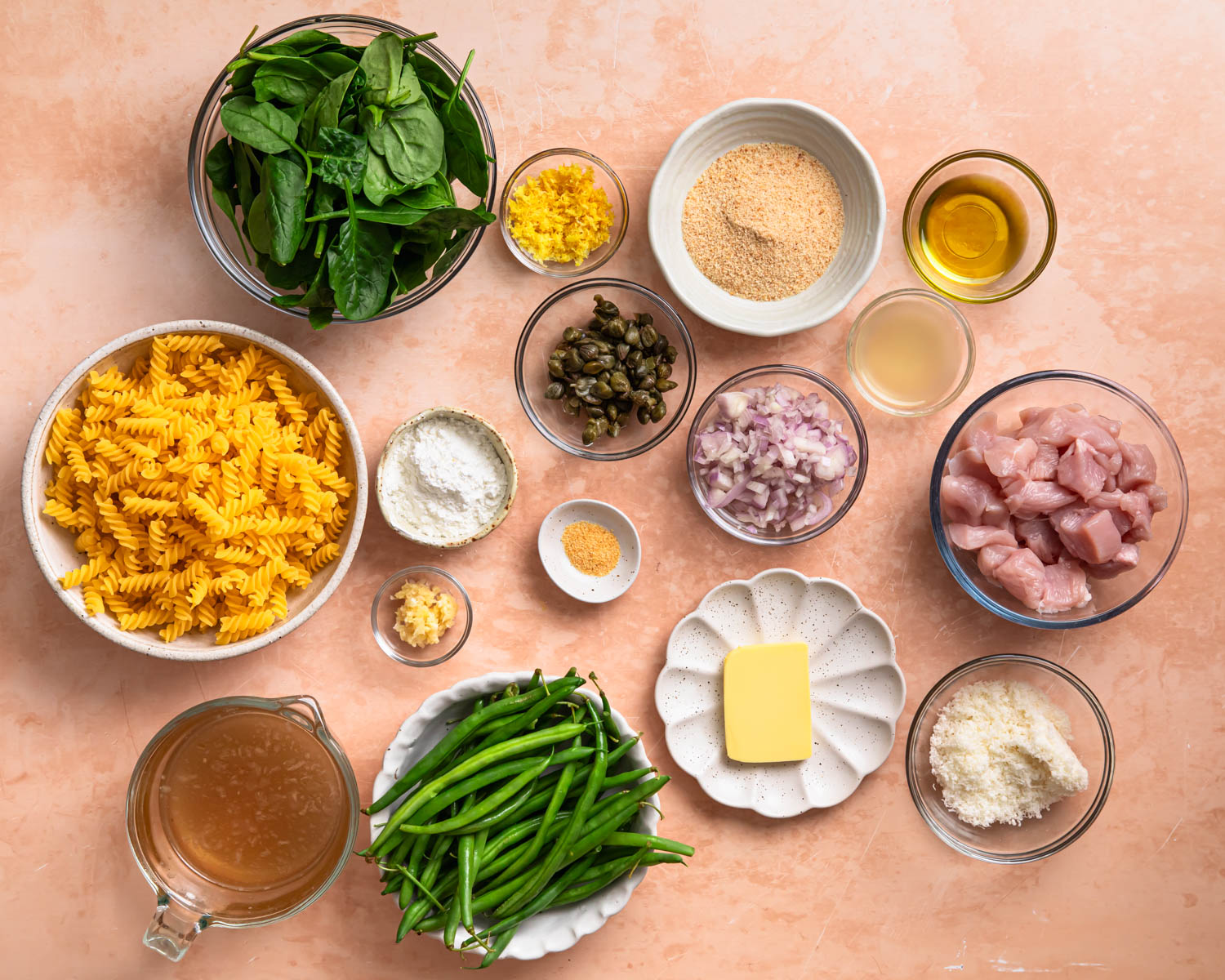 Ingredients for chicken piccata pasta laid out in individual bowls.