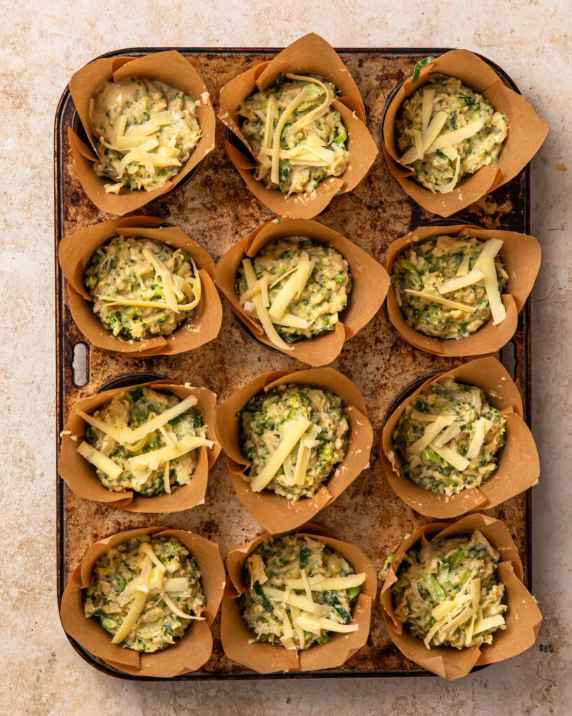 Uncooked gluten free savoury muffins topped with grated cheddar cheese.