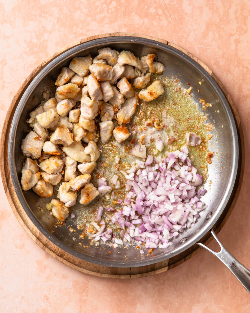 Shallots added to a pan of cooked chicken.
