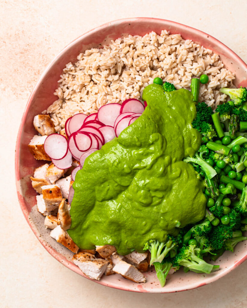 Dressing poured over orzo salad ingredients in a large salad bowl.