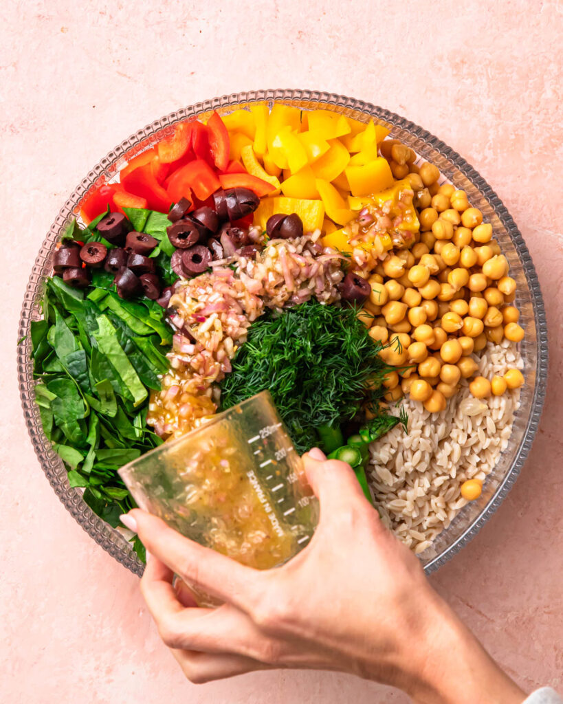 Salad dressing being poured over Mediterranean Orzo Salad.