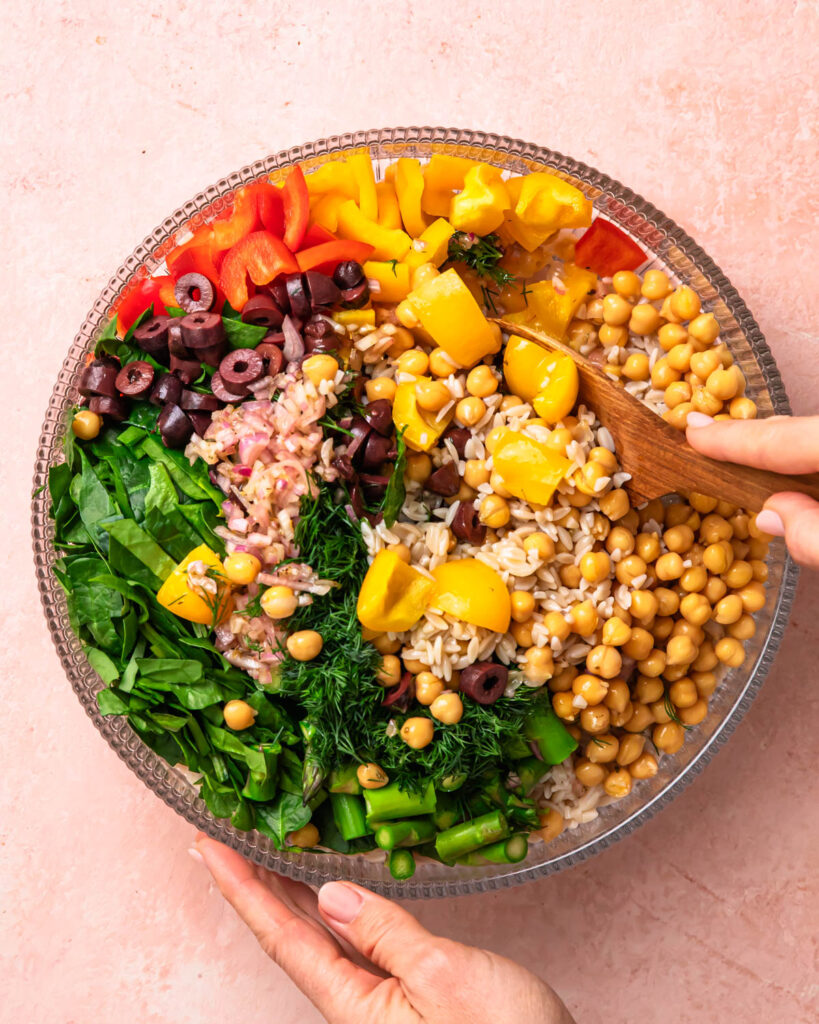 Mediterranean Orzo Salad being tossed together in a large bowl.