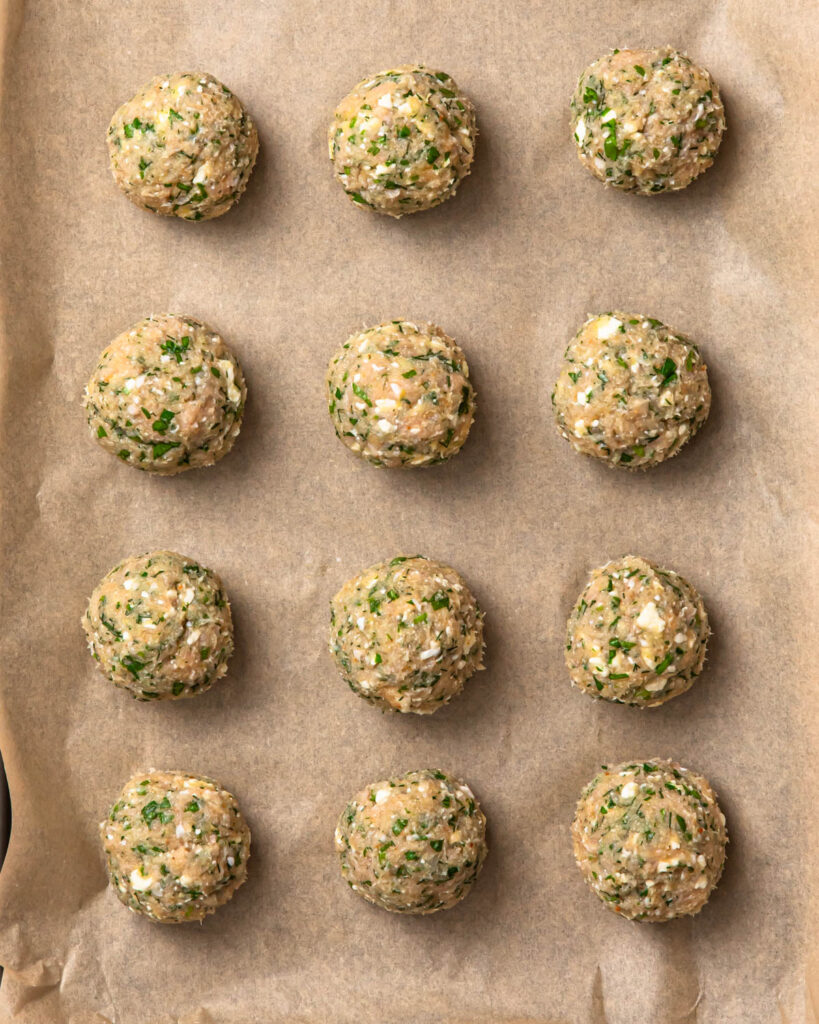 Uncooked, Greek chicken meatballs on a baking tray.