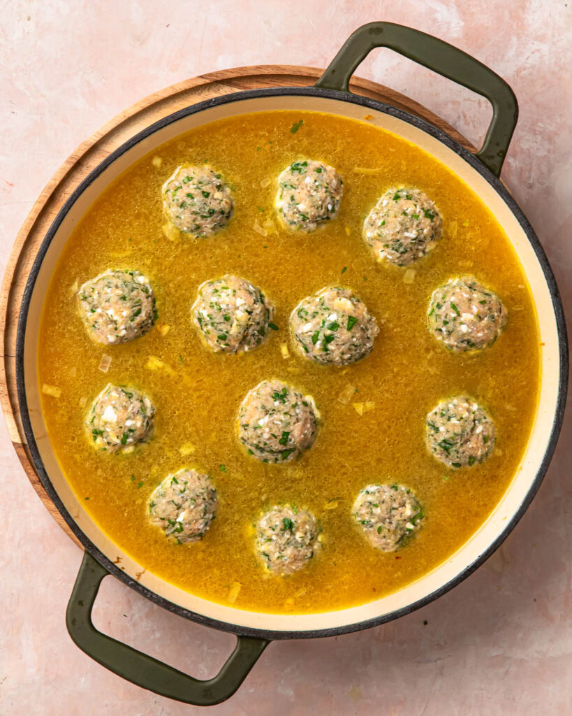 Greek chicken meatballs added to a pan of rice and broth.
