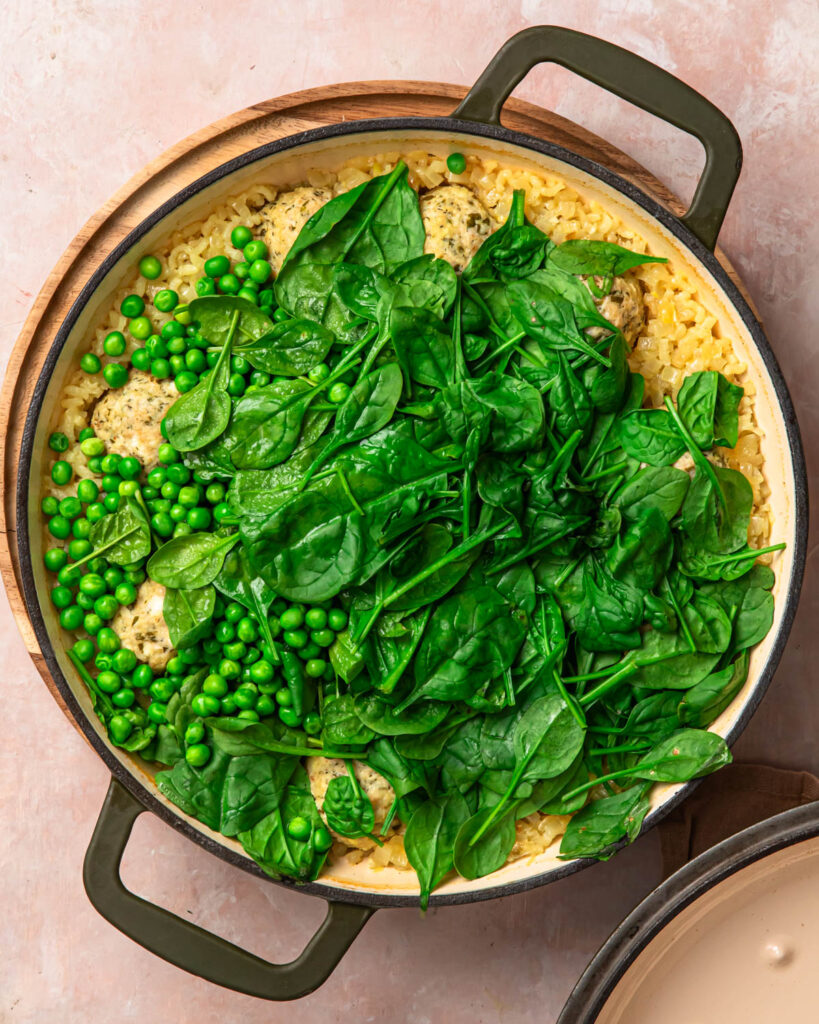 Baby spinach and peas added to a pan of cooked Greek chicken meatballs and rice. 