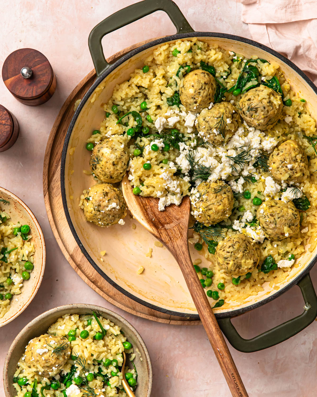 A wooden serving spoon in a pan of Greek chicken meatballs with rice and feta.