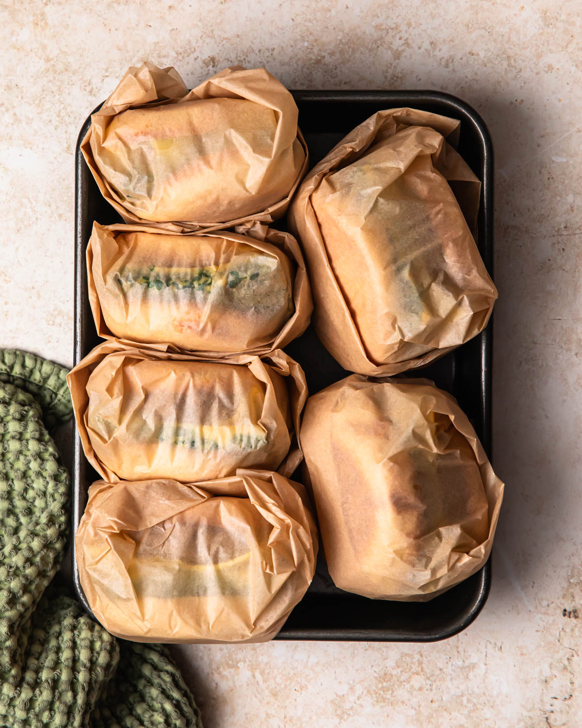 Breakfast sausage sandwiches wrapped in parchment paper and stacked in a tray.