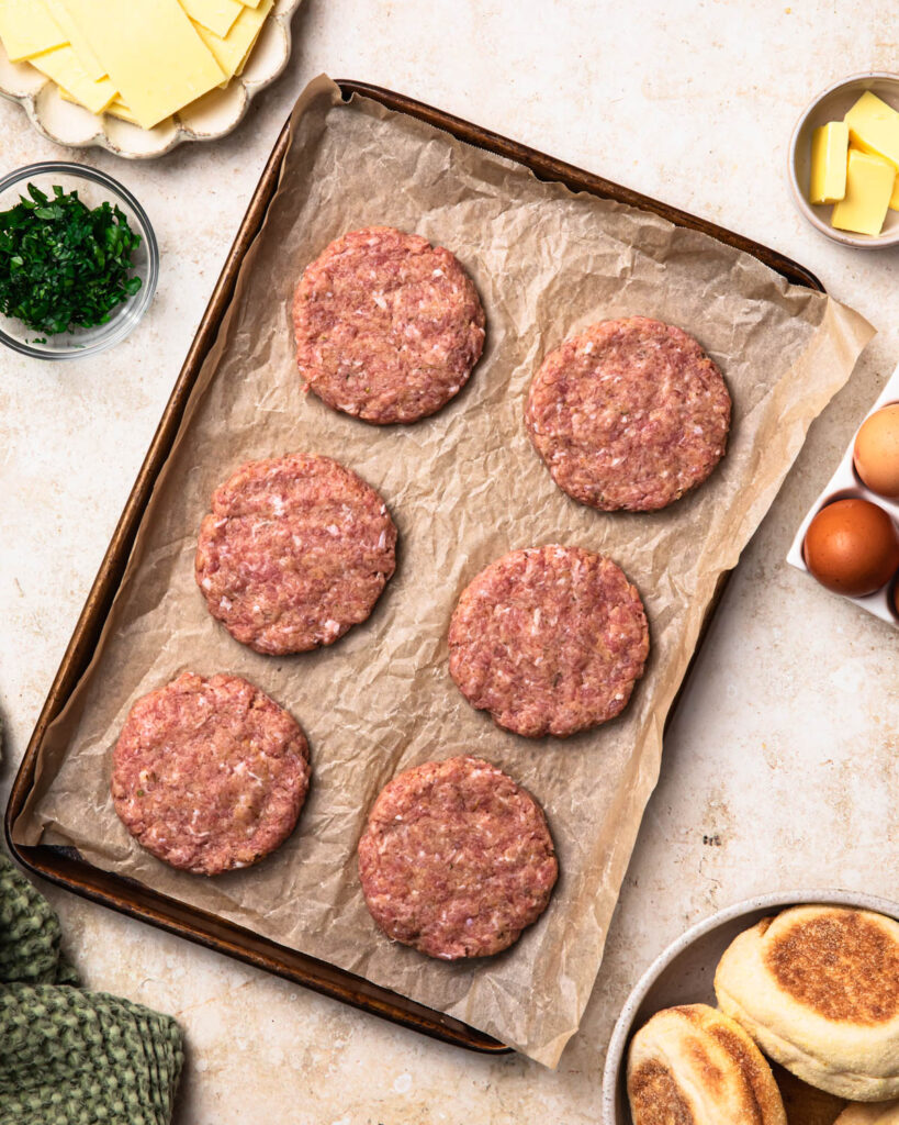 Ground sausage mixture made into patties and arranged on a baking tray.