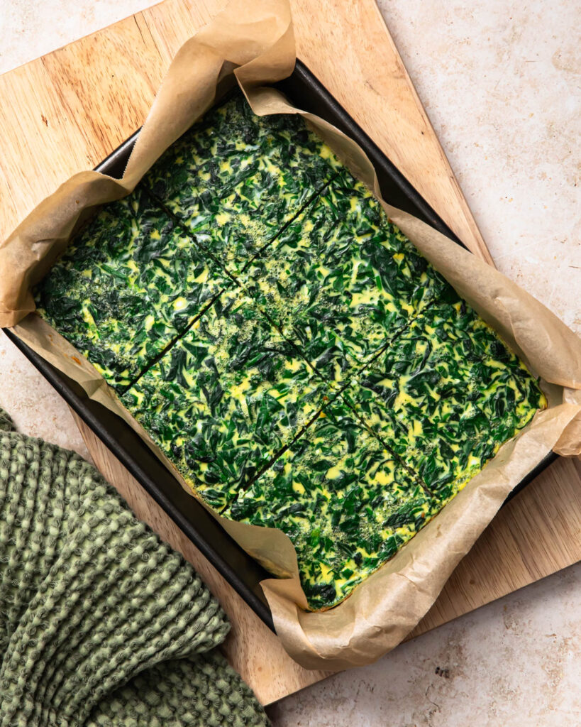 Baked eggs and spinach in a tray ready to be sliced and added to breakfast sausage sandwiches. 