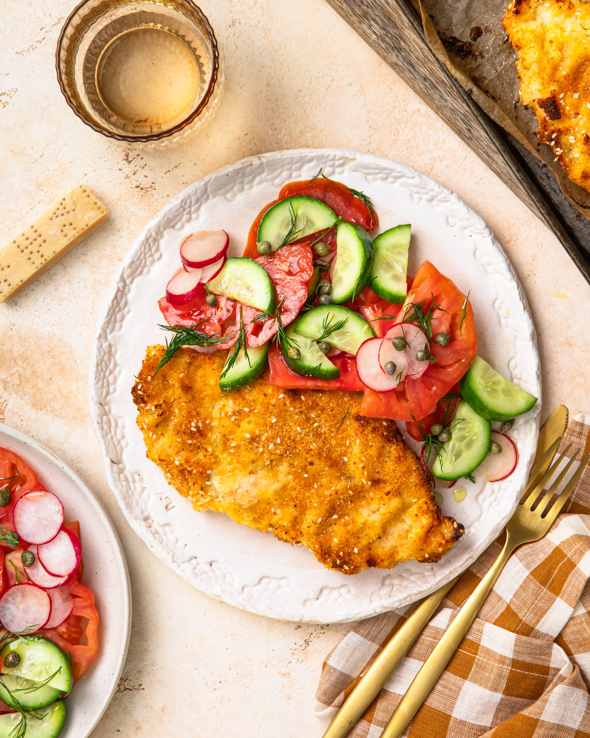 Baked parmesan breaded chicken on a plate with a tomato cucumber salad on the side.