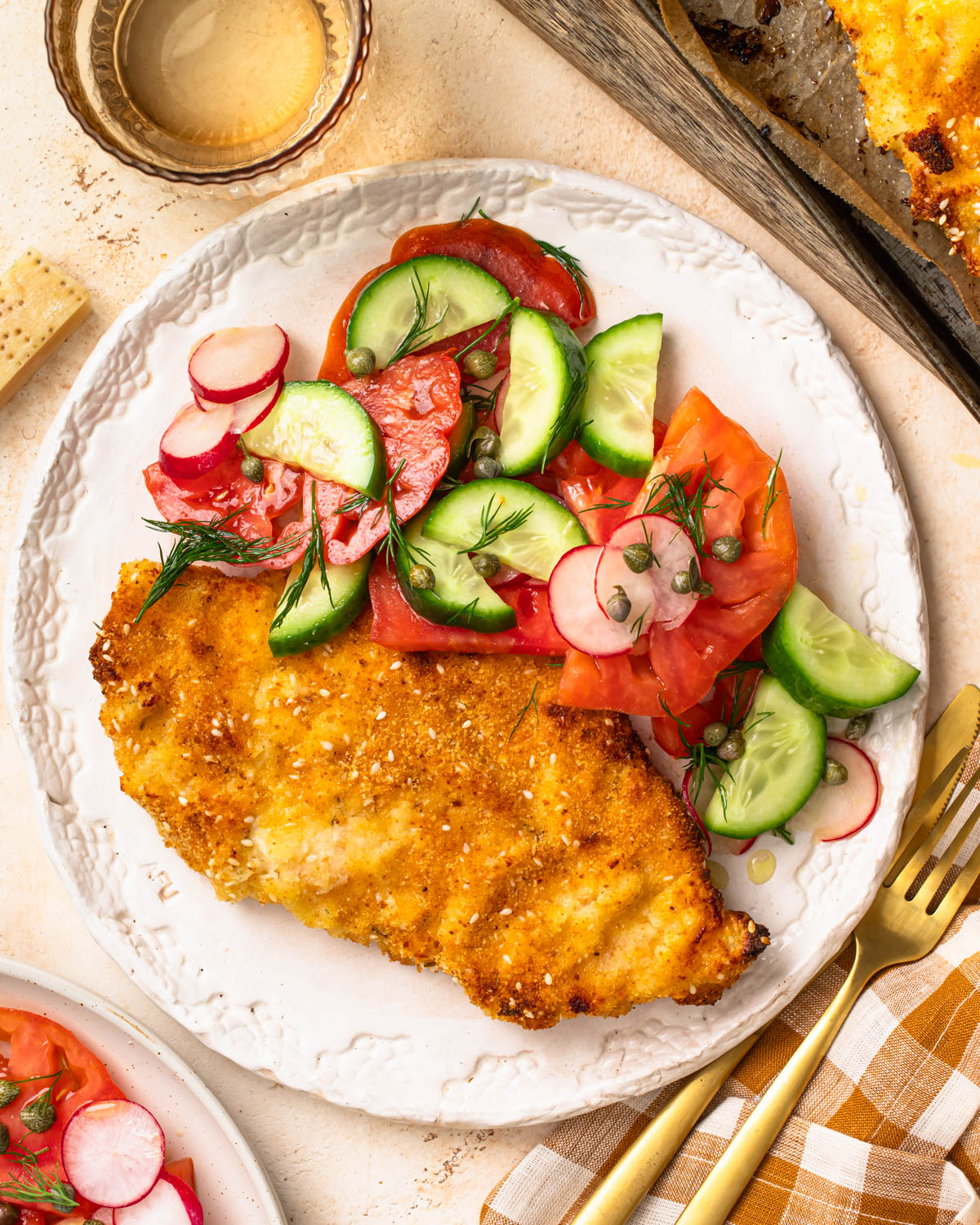 Parmesan breaded chicken served on a plate with a cucumber and tomato salad on the side.