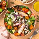 Assembled honey mustard chicken salad with sweet potatoes, avocado, red onion, and feta.