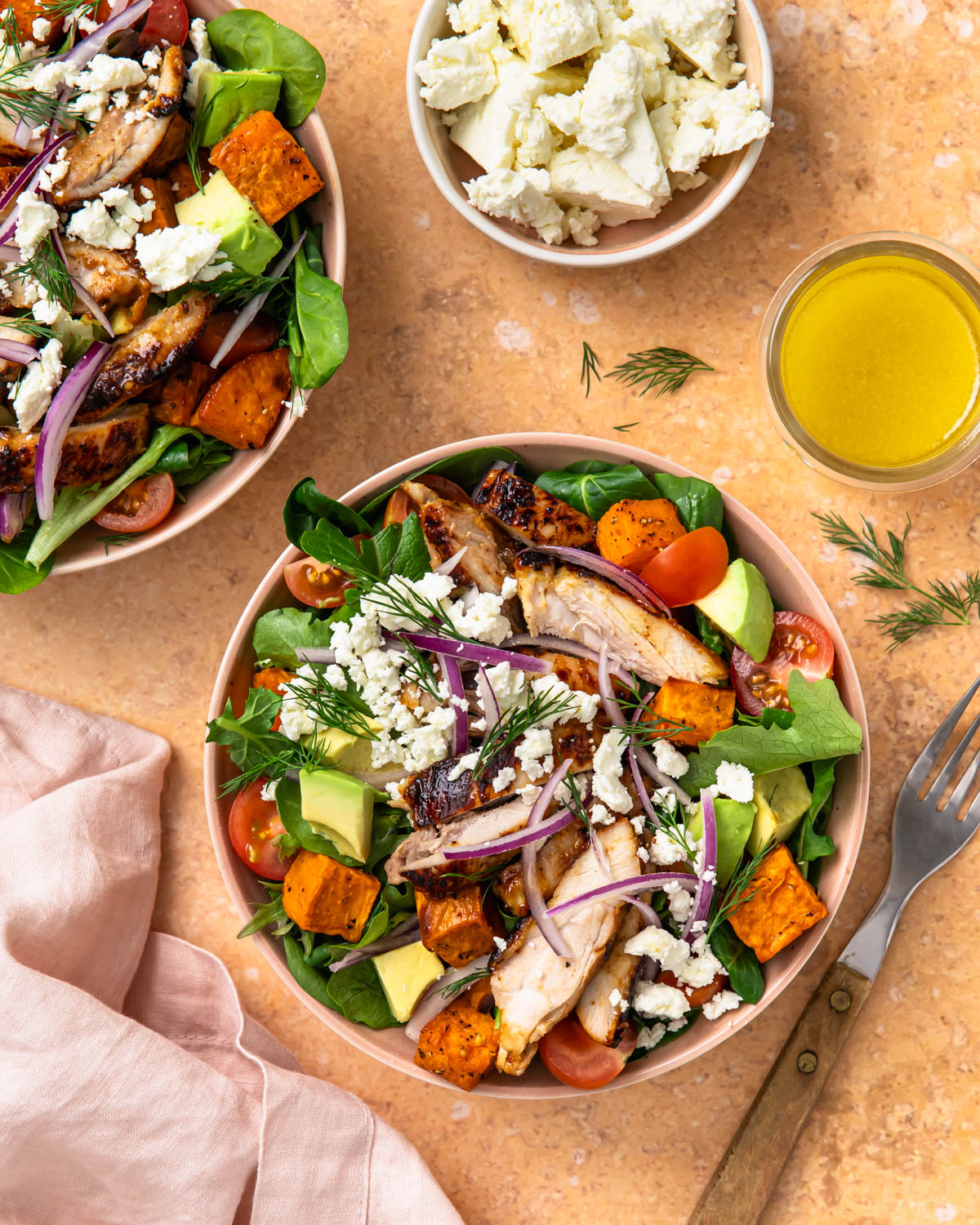 Two honey mustard chicken salad bowls next to crumbled feta and vinaigrette.