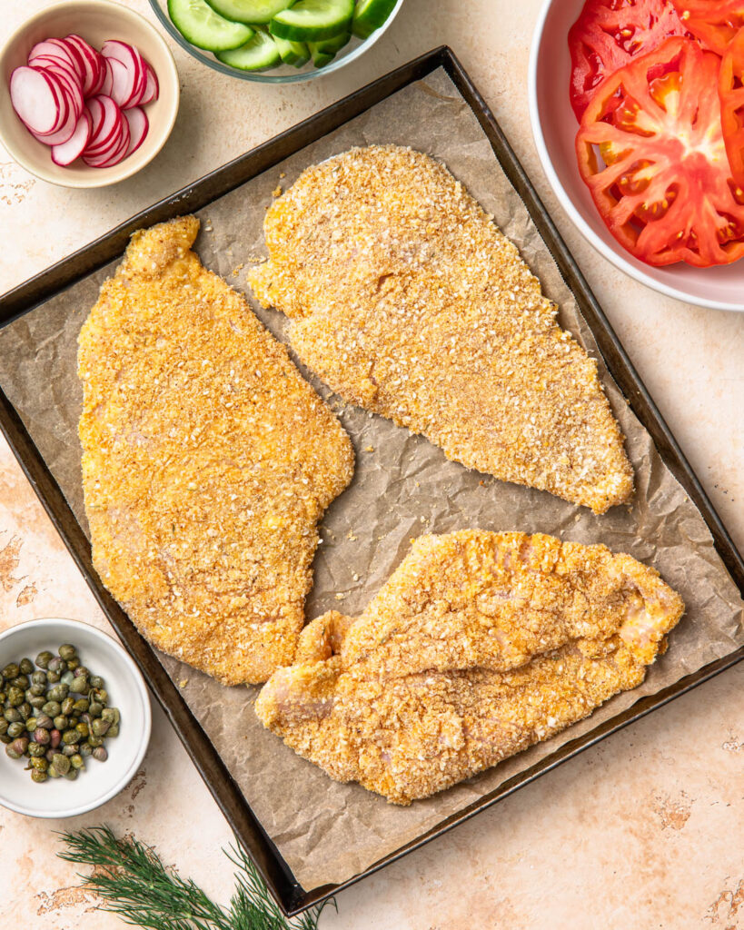 Breaded chicken bread cutlets on a sheet pan before baking.