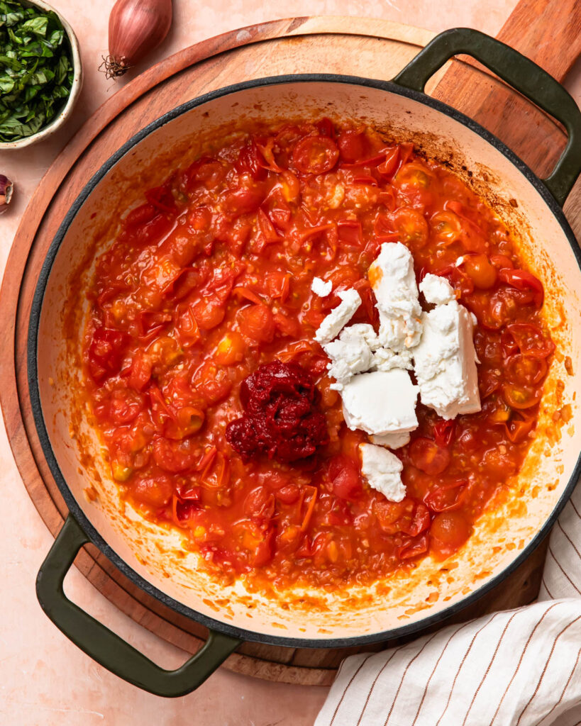 Goat's cheese and tomato paste added to the cooked cherry tomatoes in a skillet.