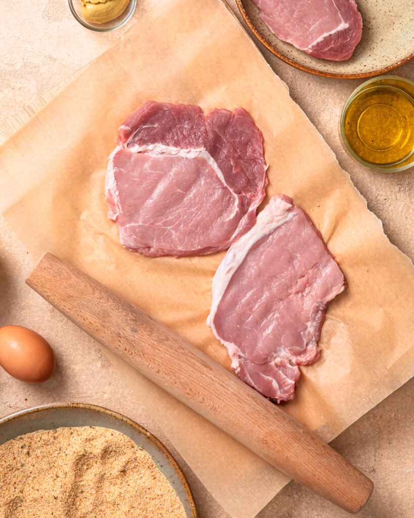 Pork medallions tenderised on a piece of baking paper.
