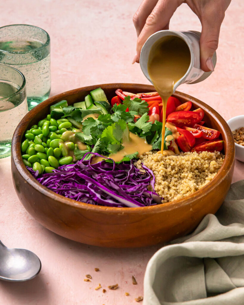 Side view of pouring miso dressing over the quinoa and veggies in a bowl.