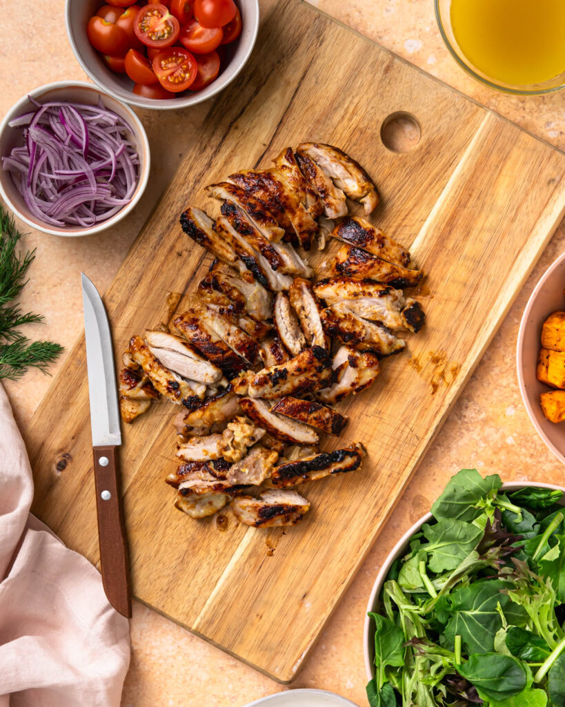 Cooked and sliced chicken thighs on a wooden cutting baord.