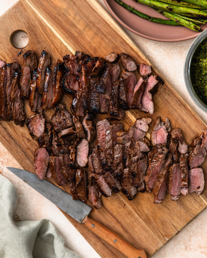 Grilled and sliced lamb rump on a wooden cutting board.