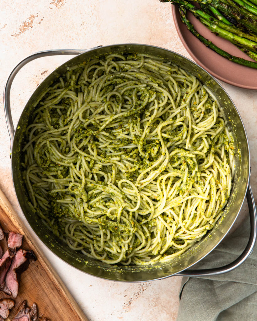 Pistachio pesto mixed with cooked spaghetti noodles in a pot.