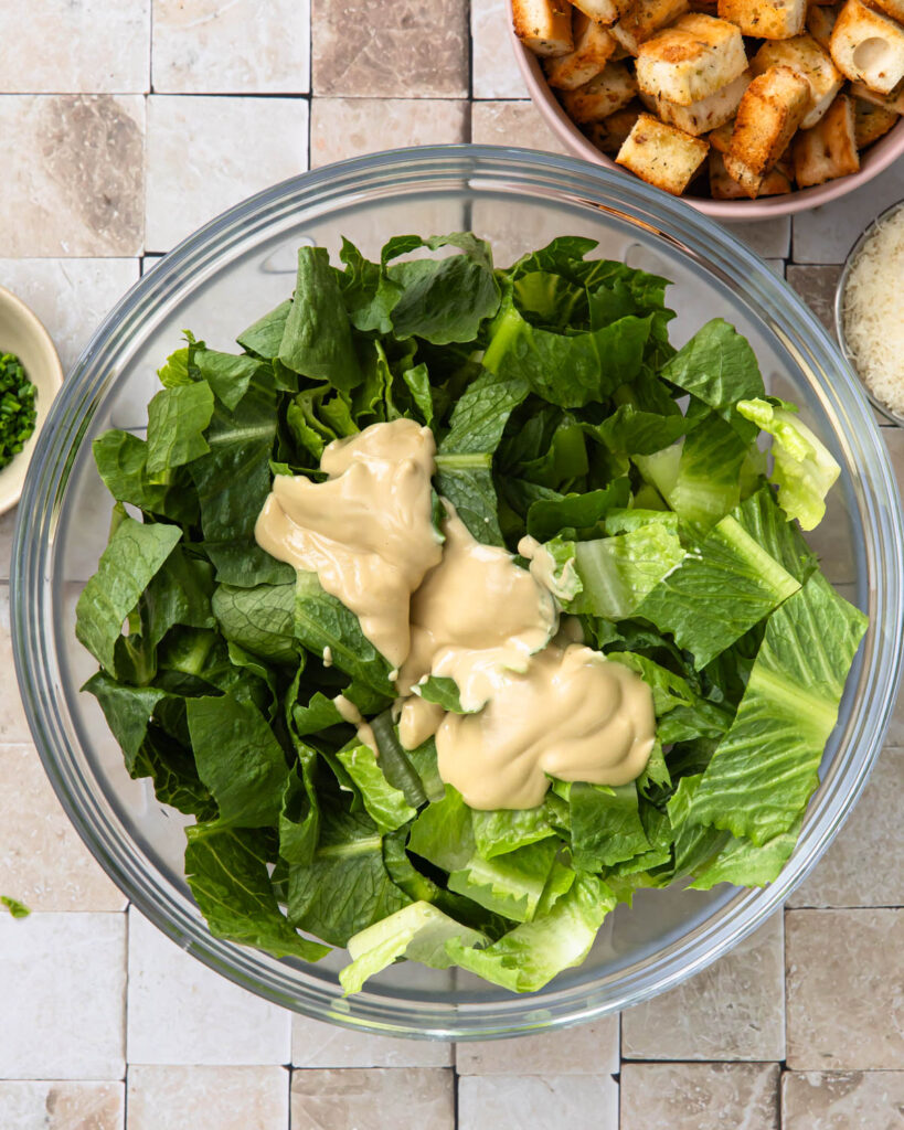 Romaine lettuce in a bowl with tahini caesar dressing on top.