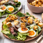 Steak caesar salad served on a plate with croutons and boiled egg.