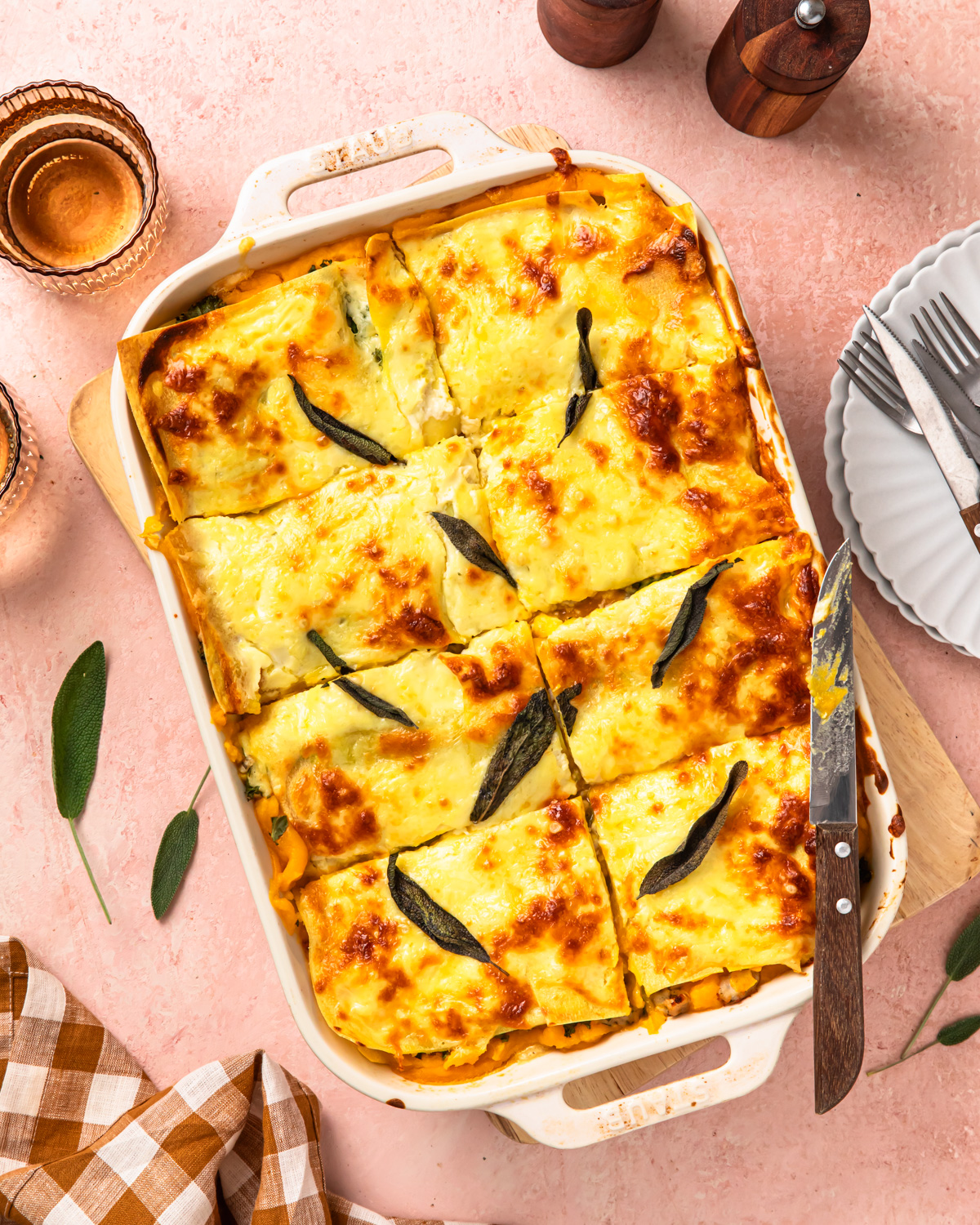 Butternut squash lasagne topped with sage leaves, in a baking dish, sliced.
