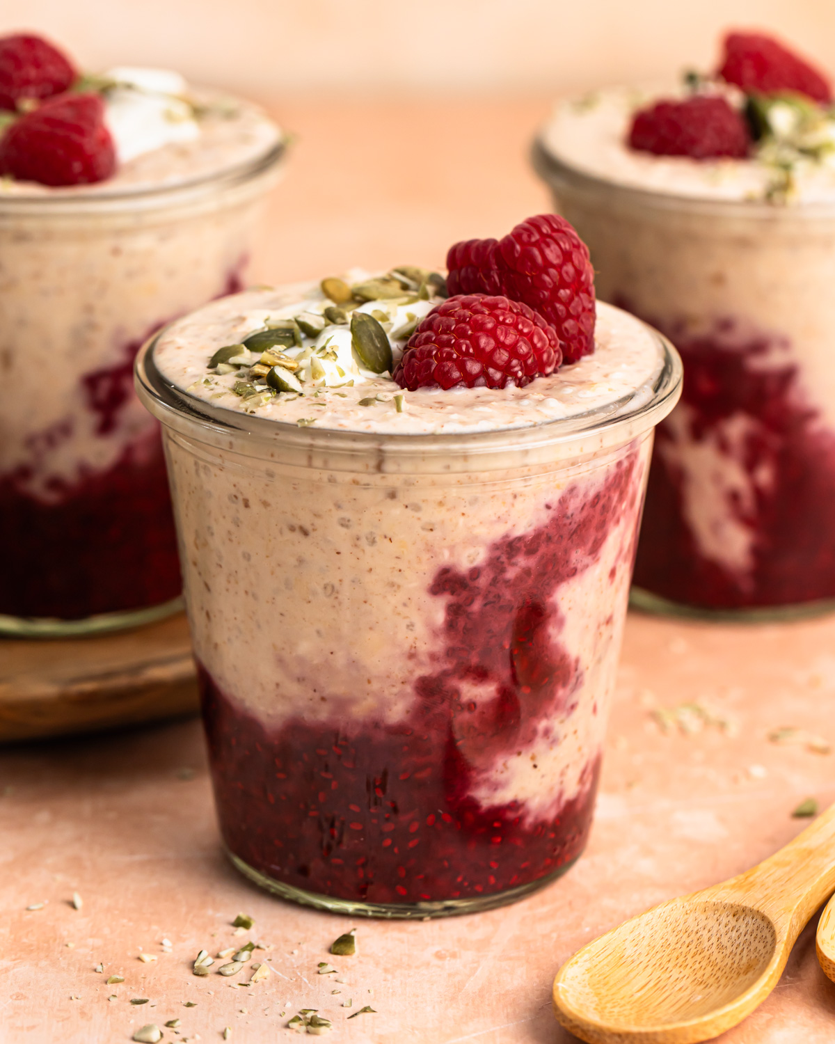 A front on photo of high protein overnight oats in a jar topped with raspberries, yoghurt and pepitas.