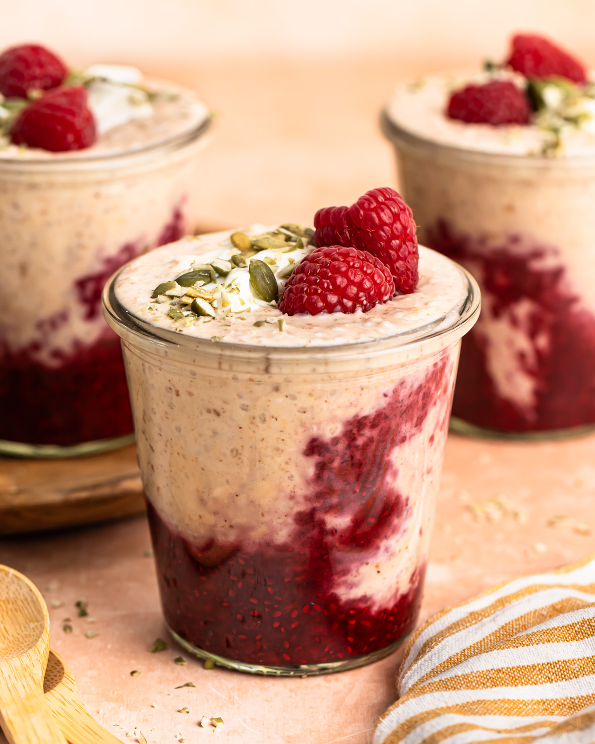 A front on photo of high protein overnight oats in a jar topped with raspberries, yoghurt and pepitas.