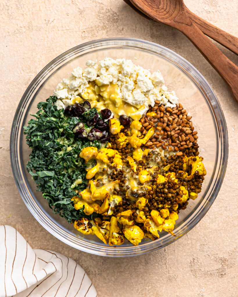 Roasted lentils and cauliflower in a bowl with kale, feta, and dressing poured over the top.