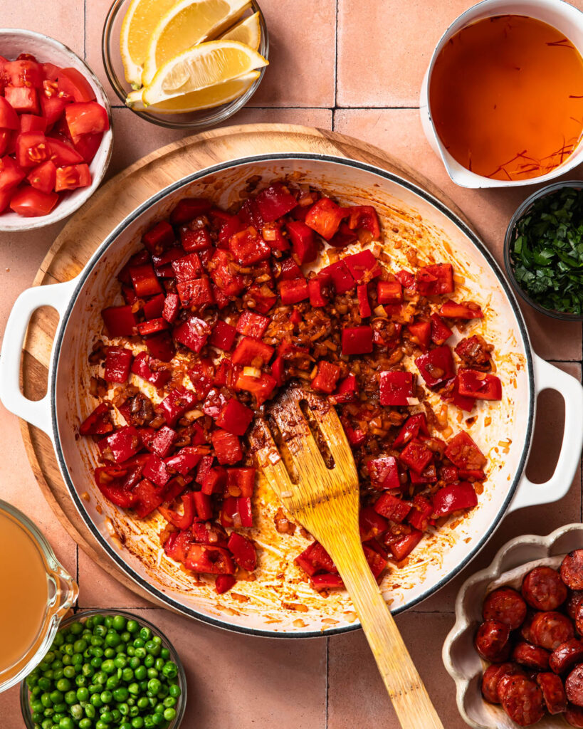 Red bell peppers and onions in a skillet with spices added.