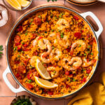 Finished oven baked paella with shrimp, served with lemon wedges.